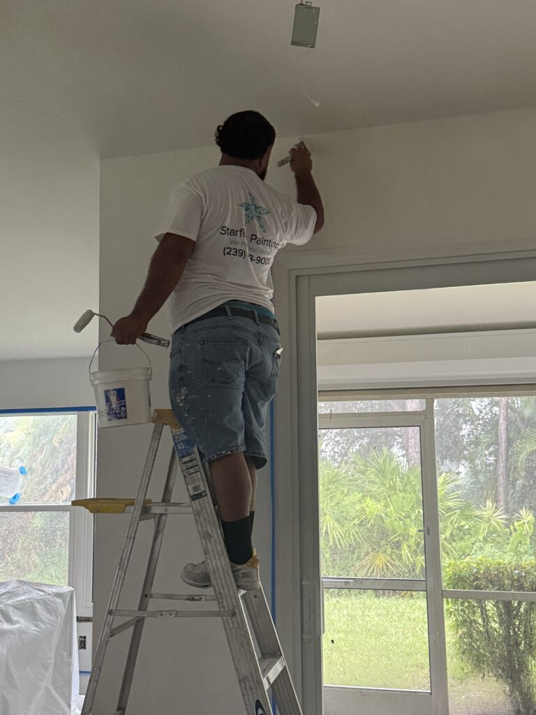 A professional painter from Starfish Painting on a ladder, meticulously painting a white interior ceiling.